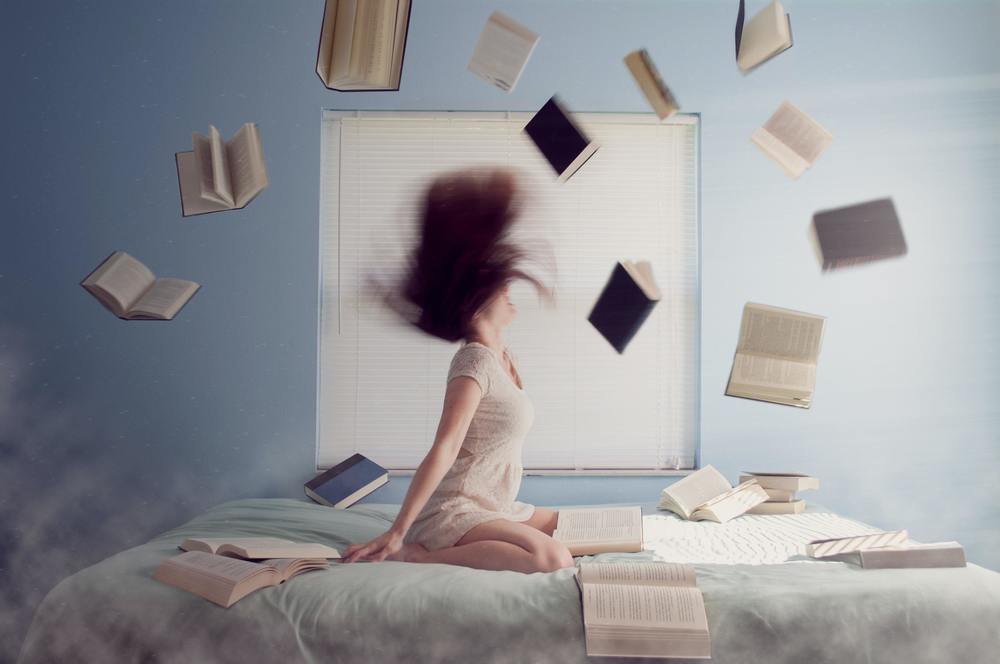 Person throwing books into the air on a bed